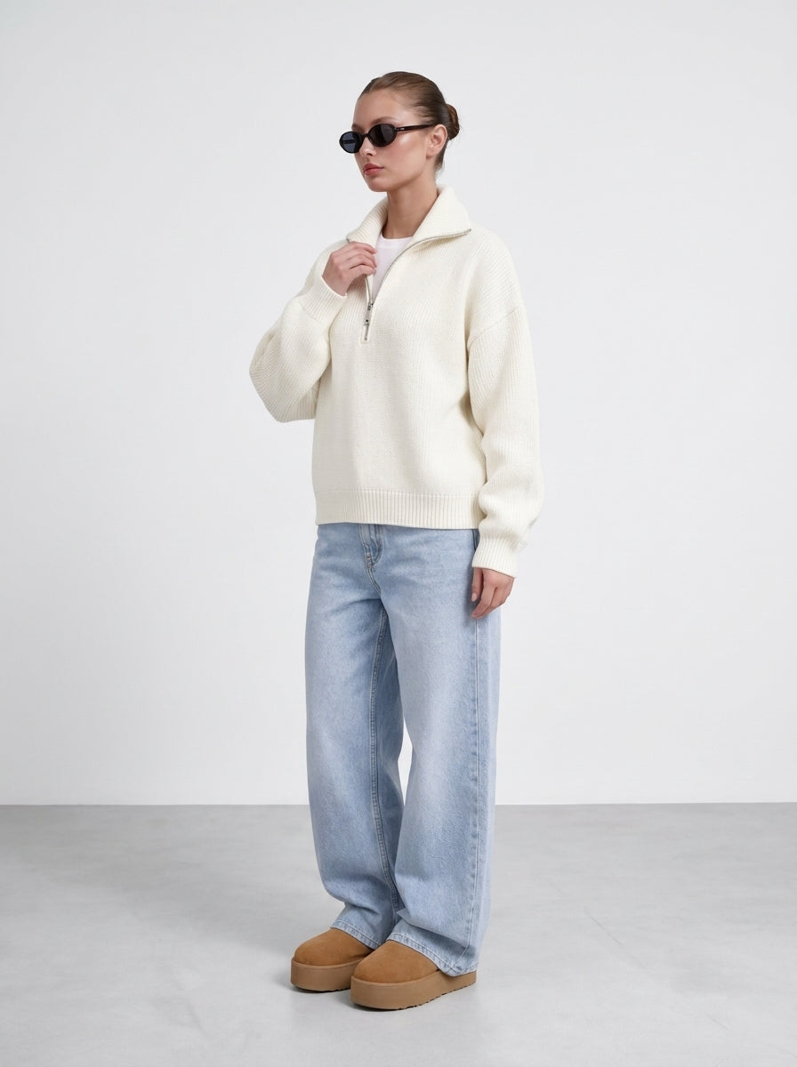 Pull demi-zip écru porté de trois quarts, main sur le col