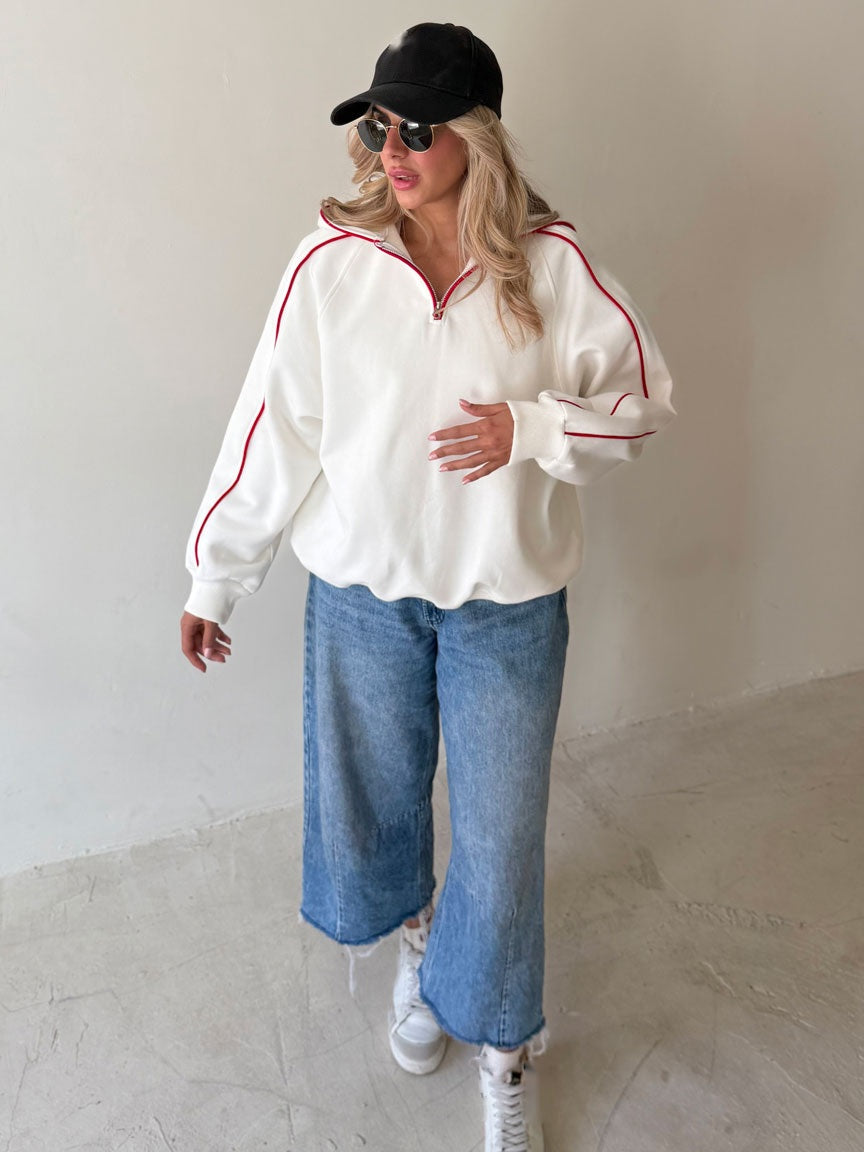 Sweat demi-zip blanc cassé à passepoil rouge porté avec un jean large