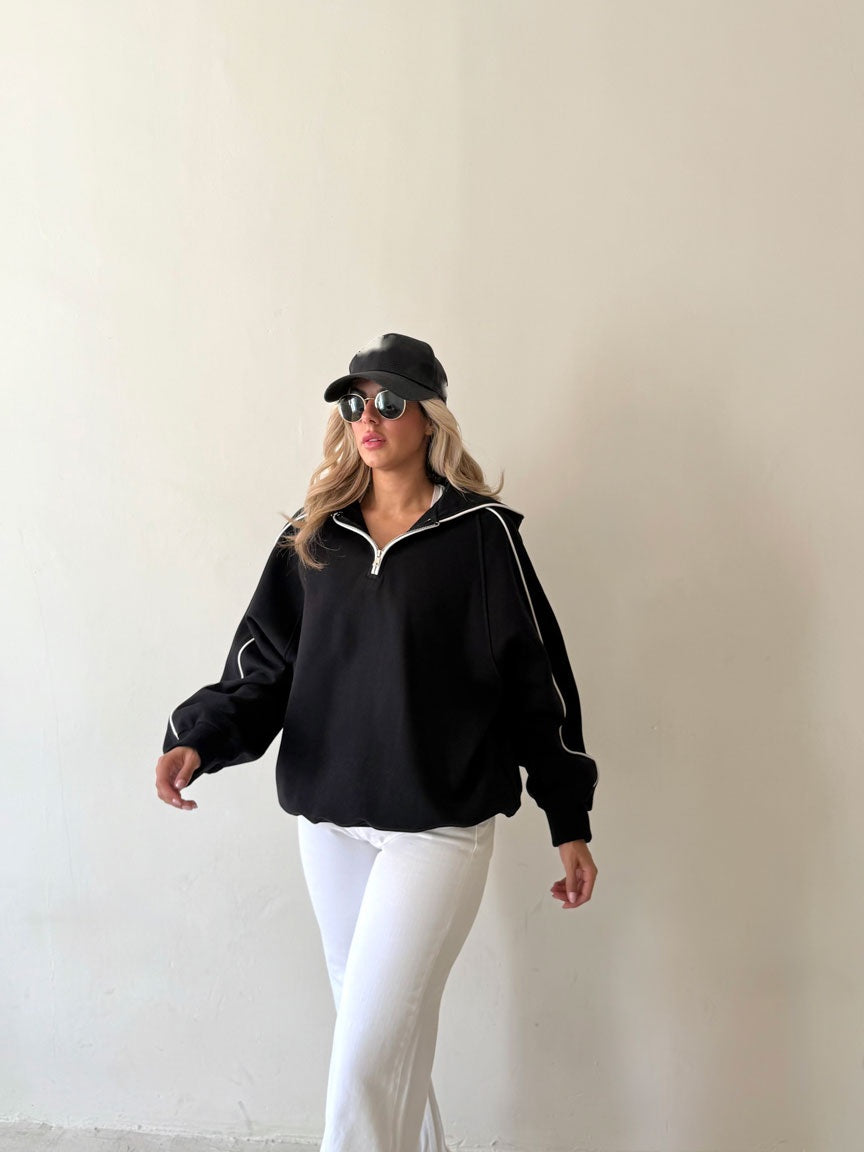 Sweat demi-zip noir à passepoil blanc porté avec un pantalon blanc